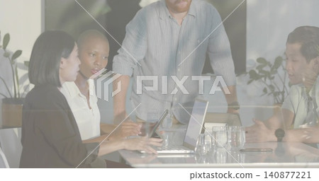 Leading facilitator leaning on glass meeting table in office, team in business attire using laptops Leading facilitator leaning on glass meeting table in office, team in business attire using laptops 140877221