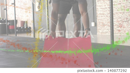 Unrolling athletic man smoothing red mat on rubber gym tiles, wearing gray shirt and dark shorts Unrolling athletic man smoothing red mat on rubber gym tiles, wearing gray shirt and dark shorts 140877292