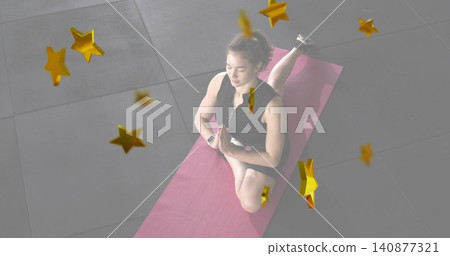 Kneeling woman in black sportswear praying on pink mat in gym, with smartwatch, shoe, gold stars Kneeling woman in black sportswear praying on pink mat in gym, with smartwatch, shoe, gold stars 140877321