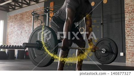 Lifting man gripping loaded barbell at gym, yellow powder trailing, wearing dark tee Lifting man gripping loaded barbell at gym, yellow powder trailing, wearing dark tee 140877327