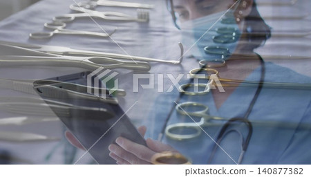 Holding tablet, female clinician in blue scrubs reviewing notes in OR prep, with instruments, mask Holding tablet, female clinician in blue scrubs reviewing notes in OR prep, with instruments, mask 140877382