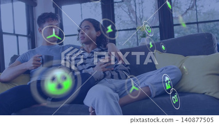 Sitting couple wearing blue tee and striped hoodie in living room, with mugs, showing AR icons Sitting couple wearing blue tee and striped hoodie in living room, with mugs, showing AR icons 140877505