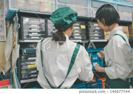 Two staff members, seen from behind, checking shelves in the back room. 140877544