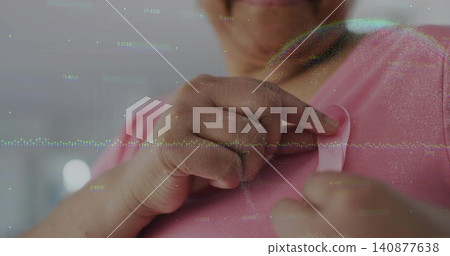 Pinning woman adjusting pink ribbon with hands on chest at home, pink shirt and data overlay Pinning woman adjusting pink ribbon with hands on chest at home, pink shirt and data overlay 140877638
