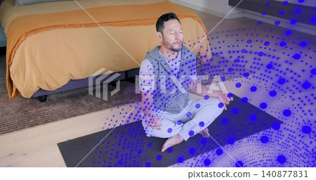 Sitting Asian man meditating on yoga mat in bedroom beside orange duvet bed, with blue overlay Sitting Asian man meditating on yoga mat in bedroom beside orange duvet bed, with blue overlay 140877831