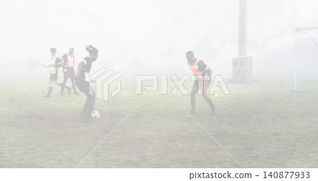 Handling ball, left player dribbling as right defender crouching on foggy pitch with cones, pinnies 140877933