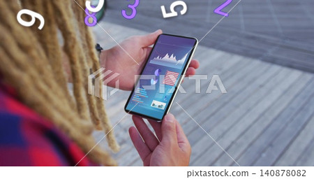 Holding smartphone, man with dreads in plaid shirt viewing data charts, numeric overlays on deck 140878082
