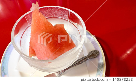A juicy watermelon in a glass container on a red table. A juicy watermelon in a glass container on a red table. 140878238