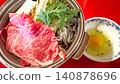 A sukiyaki pot with marbled beef and a raw egg is placed on a red table. 140878696