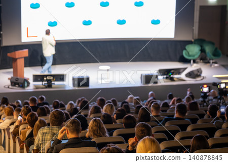 Conference presentation on stage with speaker and attentive audience in modern auditorium Conference presentation on stage with speaker and attentive audience in modern auditorium 140878845