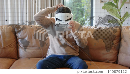 Adjusting man in beige sweatshirt placing white VR headset at home on sofa, with map overlay Adjusting man in beige sweatshirt placing white VR headset at home on sofa, with map overlay 140879112