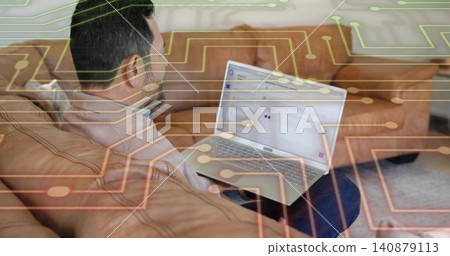 Holding laptop, Asian man reading email in living room on tan sofa, wearing pullover, tech overlay Holding laptop, Asian man reading email in living room on tan sofa, wearing pullover, tech overlay 140879113