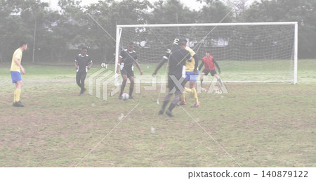 Dribbling yellow kit player advancing toward goal on muddy grass, with ball and goalkeeper gloves Dribbling yellow kit player advancing toward goal on muddy grass, with ball and goalkeeper gloves 140879122