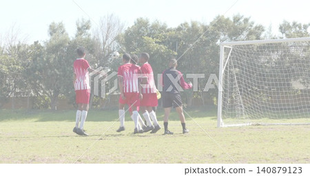 Jumping soccer players in red-white jerseys forming wall on grass pitch, ball near goal Jumping soccer players in red-white jerseys forming wall on grass pitch, ball near goal 140879123