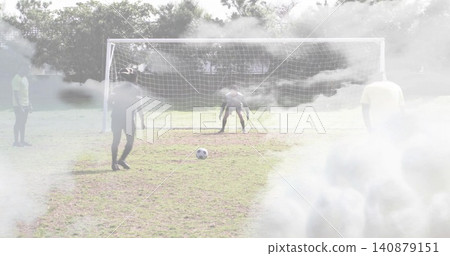 Defending soccer players in sportswear forming line on park pitch with metal goal, ball and fog Defending soccer players in sportswear forming line on park pitch with metal goal, ball and fog 140879151