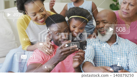 Leaning multi-gen family watching man's phone on couch at home, coral tee, social overlays, plant Leaning multi-gen family watching man's phone on couch at home, coral tee, social overlays, plant 140879250