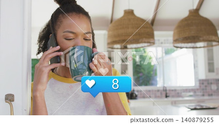 Sipping woman in gray raglan-sleeved shirt holding green mug and using phone in kitchen, copy space Sipping woman in gray raglan-sleeved shirt holding green mug and using phone in kitchen, copy space 140879255