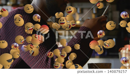 Holding smartphone, man in maroon sweater scrolling at cafe table with cup, saucer, floating emojis Holding smartphone, man in maroon sweater scrolling at cafe table with cup, saucer, floating emojis 140879257