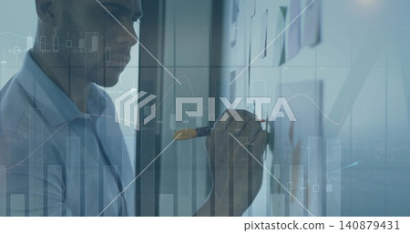 Writing man in blue shirt annotating glass at office, with orange marker and finance charts 140879431