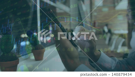 Tapping man in buttoned shirt using stylus on vertical device at shared desk, potted cacti, charts Tapping man in buttoned shirt using stylus on vertical device at shared desk, potted cacti, charts 140879434