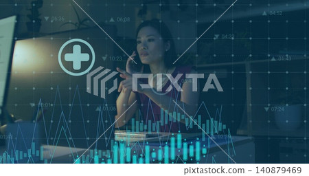 Holding phone, Chinese woman pointing at laptop and analyzing charts at dim office desk, red blouse Holding phone, Chinese woman pointing at laptop and analyzing charts at dim office desk, red blouse 140879469