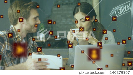 Holding tablet, plaid man chatting with grey-top woman sipping cup at cafe, laptop social-icons Holding tablet, plaid man chatting with grey-top woman sipping cup at cafe, laptop social-icons 140879507