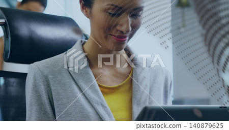Smiling woman in light gray blazer and yellow top studying laptop at office, privacy panel, chair Smiling woman in light gray blazer and yellow top studying laptop at office, privacy panel, chair 140879625