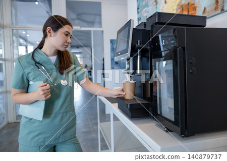 Tired female doctor making herself coffee in a hospital kitchen Tired female doctor making herself coffee in a hospital kitchen 140879737