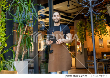 Confident barista with tablet in front of cozy cafe Confident barista with tablet in front of cozy cafe 140879935