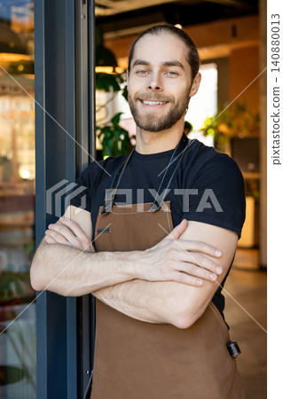Smiling handsome barista posing with crossed arms Smiling handsome barista posing with crossed arms 140880013