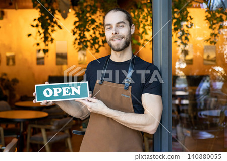 Proud owner holding green open sign leaning against entrance Proud owner holding green open sign leaning against entrance 140880055