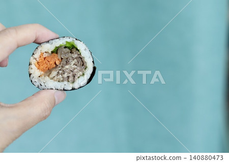 A Korean seaweed roll, bulgogi kimbap, held up in the left hand. A Korean seaweed roll, bulgogi kimbap, held up in the left hand. 140880473