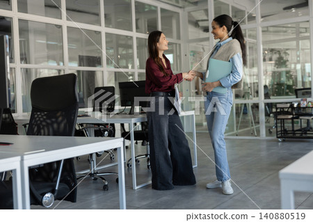 Two young female colleagues shaking hands in workspace 140880519