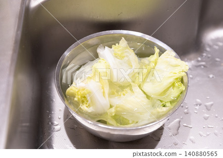 Put water into a bowl of lettuce in the kitchen. Put water into a bowl of lettuce in the kitchen. 140880565