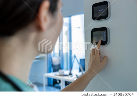 Dark-haired female doctor in lab coat setting the temperature range in a room Dark-haired female doctor in lab coat setting the temperature range in a room 140880704