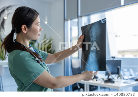 Young doctor in lab coat checking the xray result and looking focused Young doctor in lab coat checking the xray result and looking focused 140880758