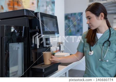 Tired female doctor making herself coffee in a hospital kitchen Tired female doctor making herself coffee in a hospital kitchen 140880774
