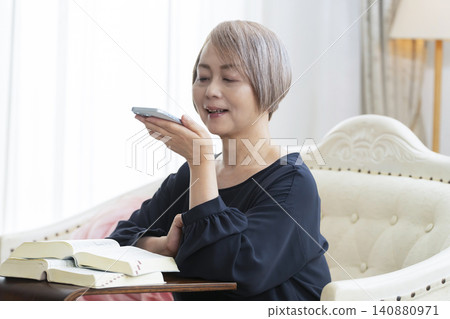 A senior woman sits on a sofa and studies English conversation on her smartphone. A senior woman sits on a sofa and studies English conversation on her smartphone. 140880971