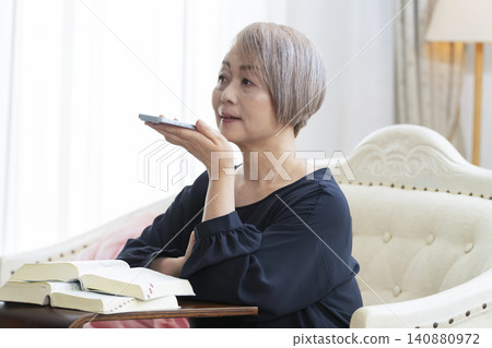 一位老婦人坐在沙發上,用智慧型手機學習英語會話。 一位老婦人坐在沙發上,用智慧型手機學習英語會話。 140880972