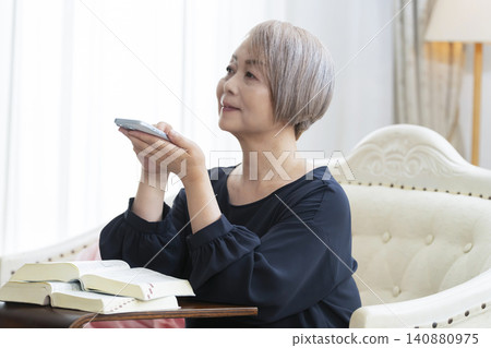 A senior woman sits on a sofa and studies English conversation on her smartphone. A senior woman sits on a sofa and studies English conversation on her smartphone. 140880975