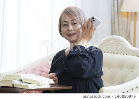 一位老婦人坐在沙發上,用智慧型手機學習英語會話。 一位老婦人坐在沙發上,用智慧型手機學習英語會話。 140880979