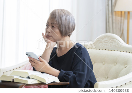A senior woman sits on a sofa and studies English conversation on her smartphone. A senior woman sits on a sofa and studies English conversation on her smartphone. 140880988