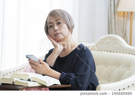 一位老婦人坐在沙發上,用智慧型手機學習英語會話。 一位老婦人坐在沙發上,用智慧型手機學習英語會話。 140880989