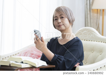 A senior woman sits on a sofa and studies English conversation on her smartphone. A senior woman sits on a sofa and studies English conversation on her smartphone. 140880992