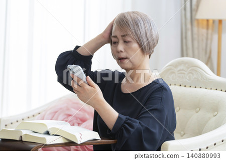 一位老婦人坐在沙發上，用智慧型手機學習英語會話。 140880993