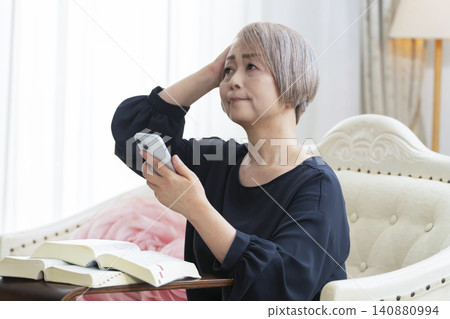 一位老婦人坐在沙發上,用智慧型手機學習英語會話。 一位老婦人坐在沙發上,用智慧型手機學習英語會話。 140880994