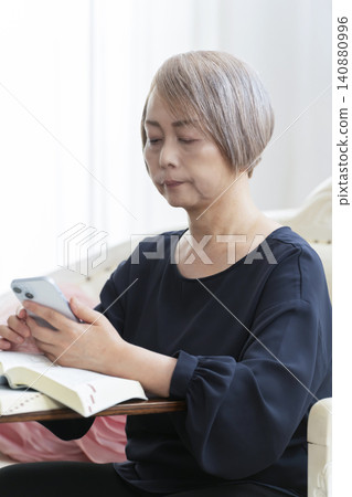 A senior woman sits on a sofa and studies English conversation on her smartphone. A senior woman sits on a sofa and studies English conversation on her smartphone. 140880996
