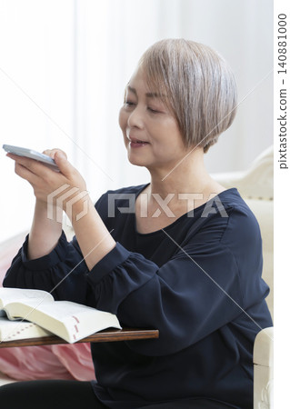 一位老婦人坐在沙發上,用智慧型手機學習英語會話。 一位老婦人坐在沙發上,用智慧型手機學習英語會話。 140881000