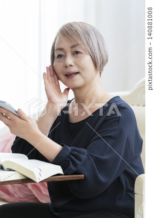 A senior woman sits on a sofa and studies English conversation on her smartphone. A senior woman sits on a sofa and studies English conversation on her smartphone. 140881008
