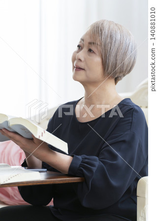 A senior woman sits on a sofa and studies English conversation on her smartphone. A senior woman sits on a sofa and studies English conversation on her smartphone. 140881010